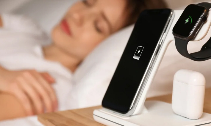 Zdjęcie przedstawia ładowarkę indukcyjną Qi2 25W 3w1 oraz kobietę śpiącą w tyle